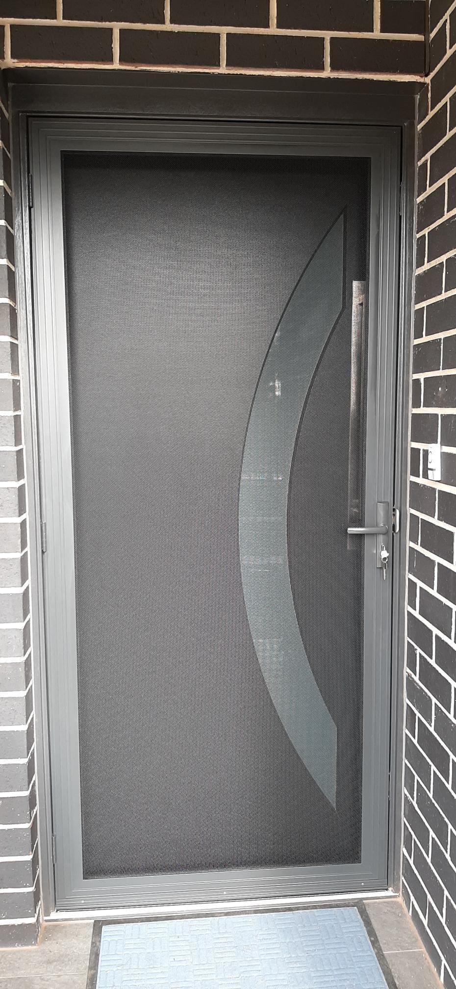 A black security screen doors adelaide with a blue mat at the entrance, showcasing Knight Shutters and Improvements branding.