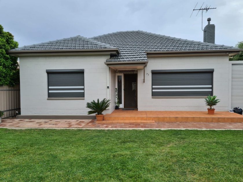 Grey aluminium roller shutters fitted to windows of a cream brick Adelaide home